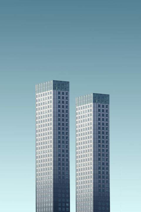 Duas torres esbeltas e idênticas, em tom azul-acinzentado, sobre fundo de céu uniforme.