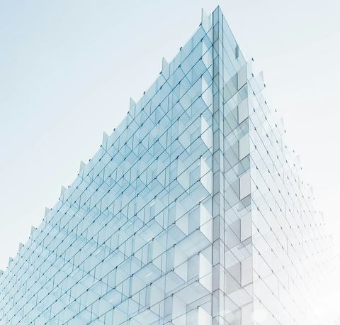 Quina de um edifício revestido por painéis de vidro em tons claros.
