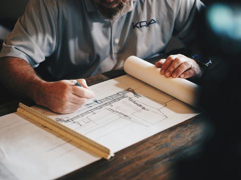 Mãos de um profissional fazendo anotações sobre uma prancha de desenho técnico.